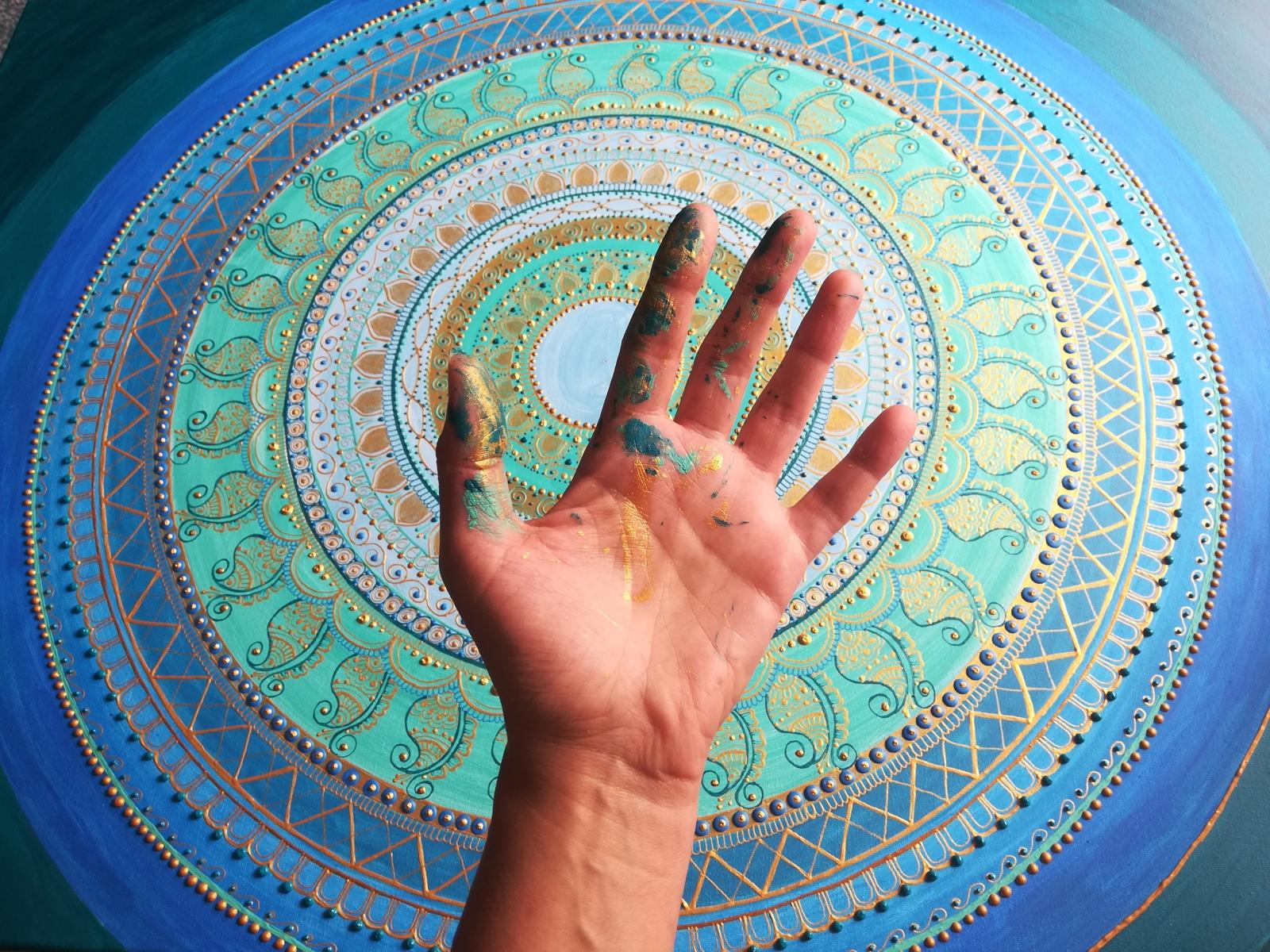 Farbbedeckte Hand vor einem blau-türkisen Mandala